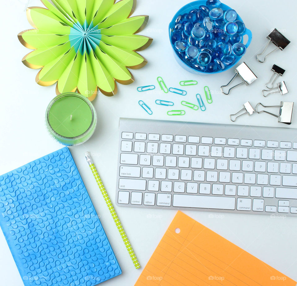 colorful stationary flat lay. The photo contains an IMac keyboard as well as colorful stationary supplies such as paper, journal, pencil, paper clips and a candle. perfect Flat lay to use for graphics to draw attention to the eyes.