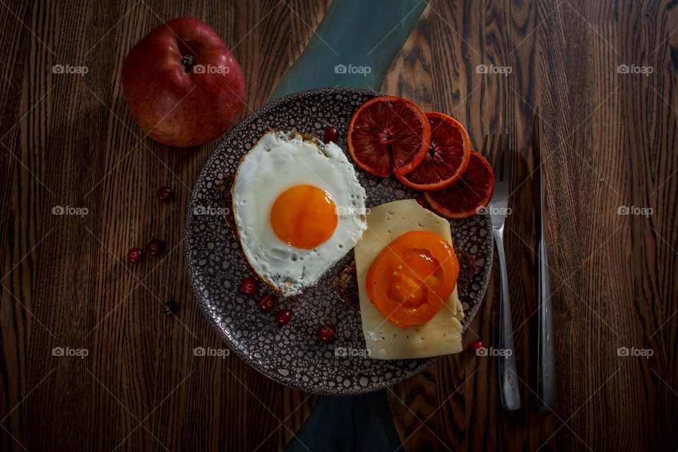 Grain bread with egg, tomato, cheese and bacon on ceramic plate with red orange to desert