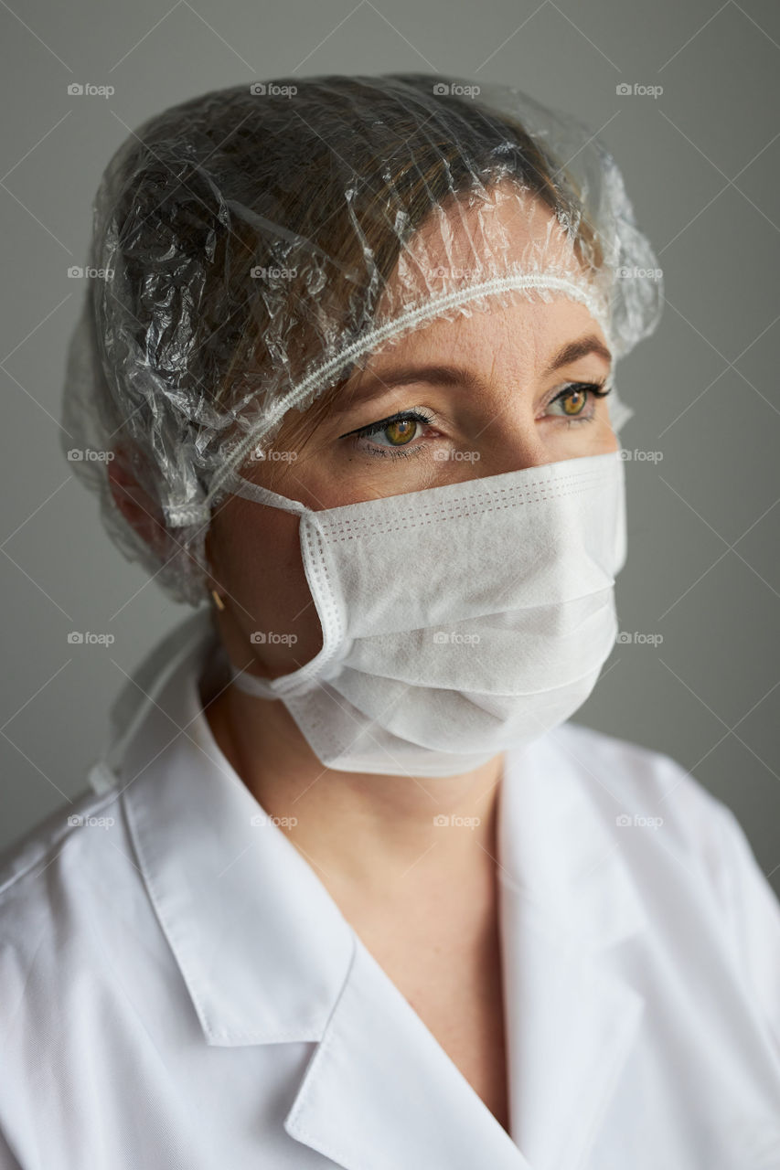 Doctor with face covered with mask. Portrait of young woman wearing the uniform, cap and mask to avoid virus infection and to prevent the spread of disease. Real people, authentic situations