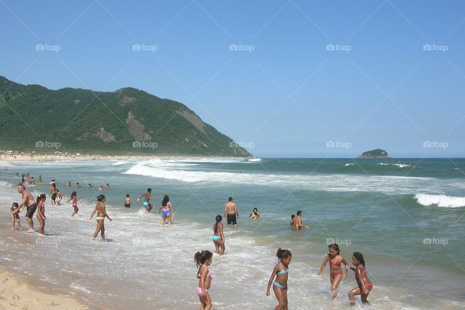 Lots of people playing in the water at the beach in Grumari Rio de Janeiro in a very sunny day