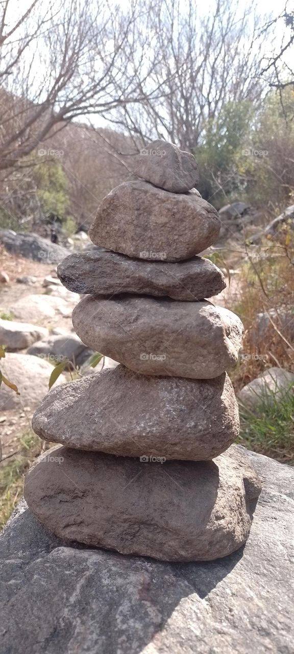 pila de piedras en camino hacia cerro de ve los árboles los arbusto y reflejo del sol