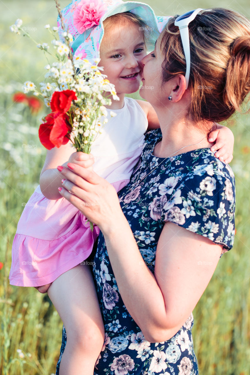 Mother and her little daughter in the field of wild flowers. Little girl picking the spring flowers for her mom for Mother's Day in the meadow. Girl handing the flowers to her mom. Nature scene, family time