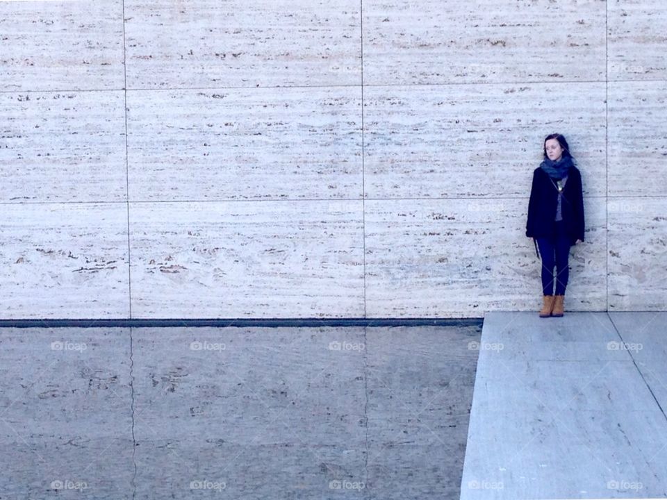 Girl standing against the smooth wall of the Barcelona Pavilion next to the reflecting pool in Barcelona, Spain. 
