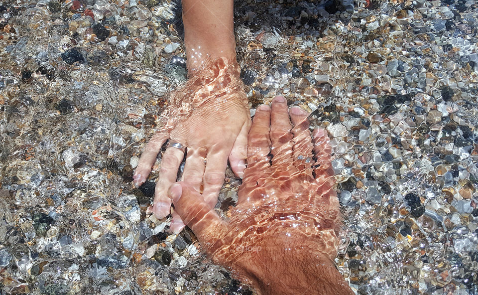 a pare of hands with the rings of married couple covered with water on the seaside