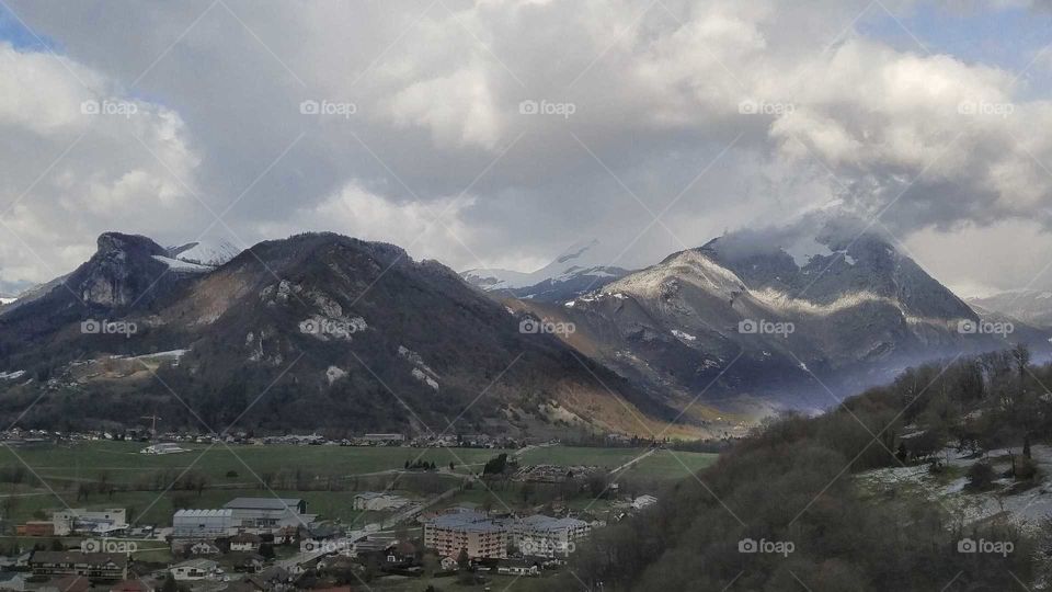 Small, old town in a valley in the French Alps with big grey and white clouds overhead.