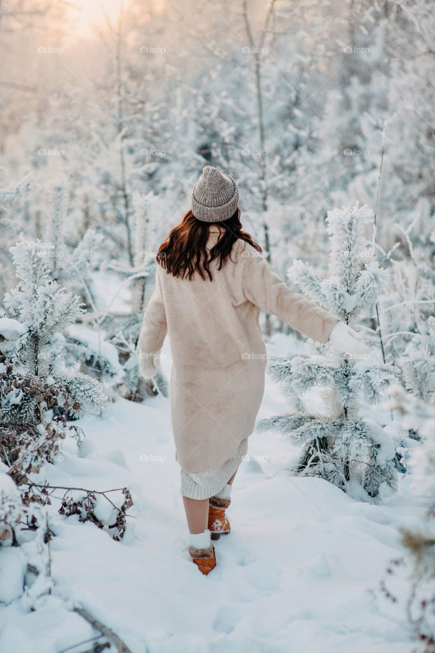 From behind. A woman in beige winter coat standing in snowy forest. Winter fairy tail. Enjoying snow