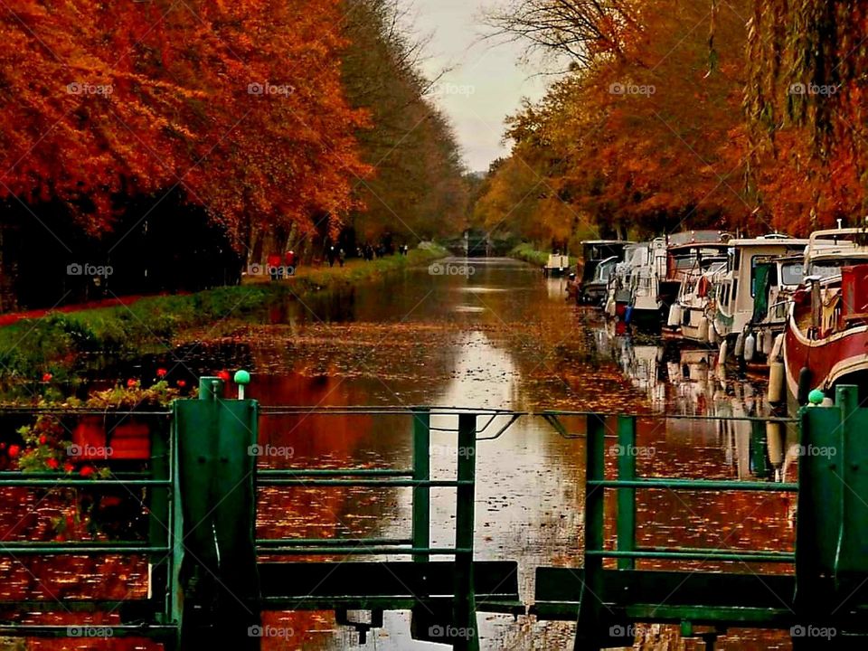 The Malestroit sluice-gate with its riverboats and its canal lined with trees adorned with their autumn colours, all reflecting on the water