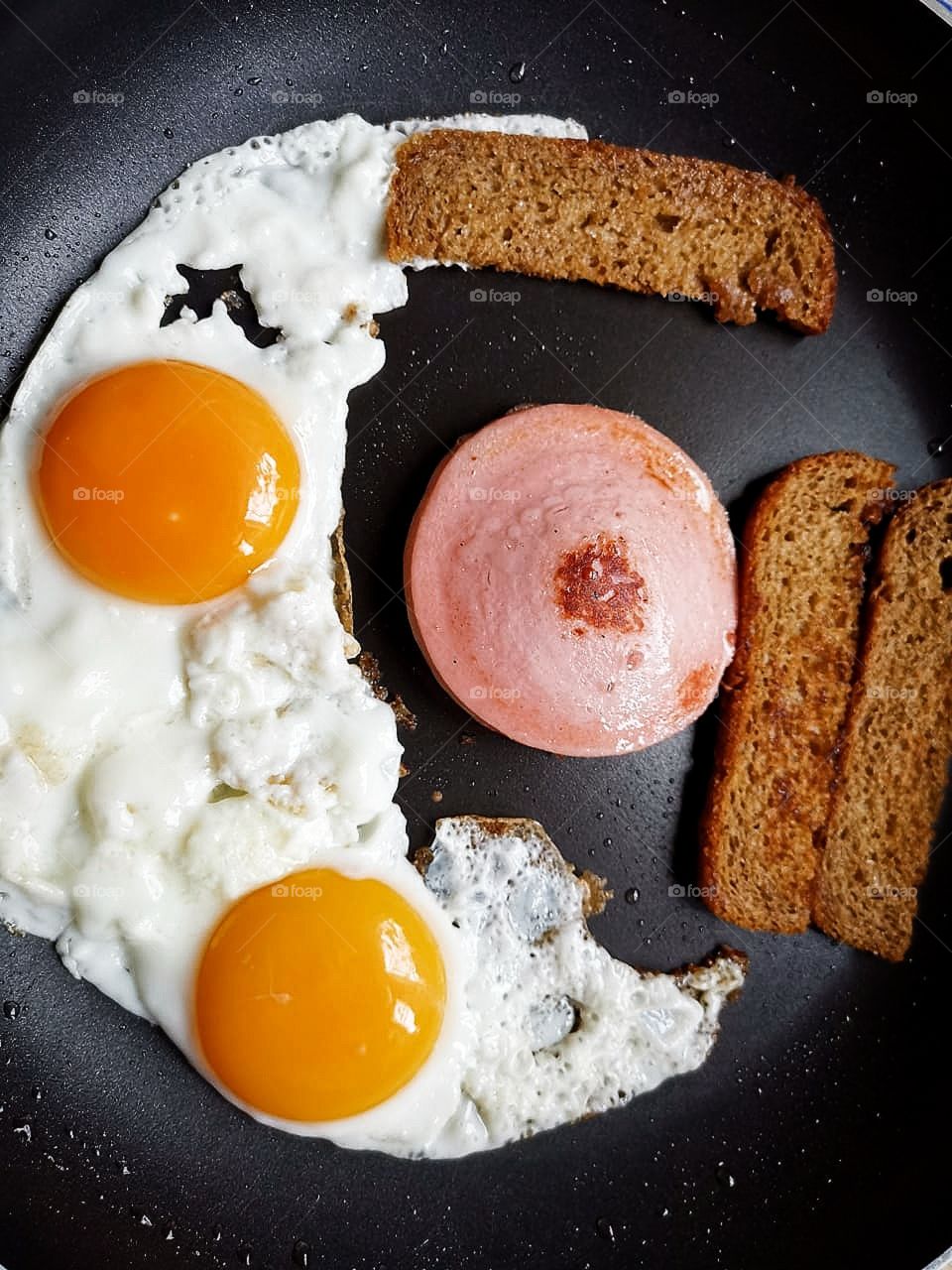 Fried eggs from two eggs, a piece of sausage and slices of toasted bread