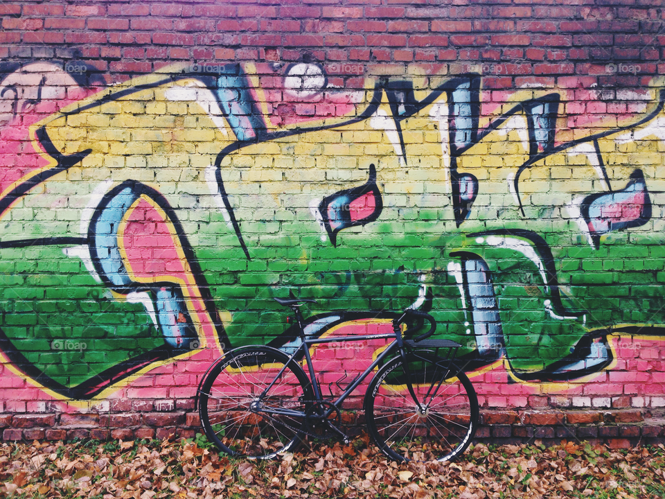 Grayish-black brakeless fixie bicycle standing in front of the wall decorated with bright colored wallart graffiti