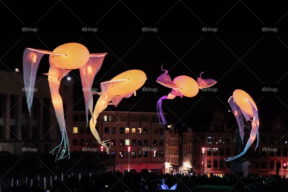 Beautiful view of the flying colorful rubber dolphins with yellow lilac backlight on the square in the night city of Brussels in Belgium, close-up side view.