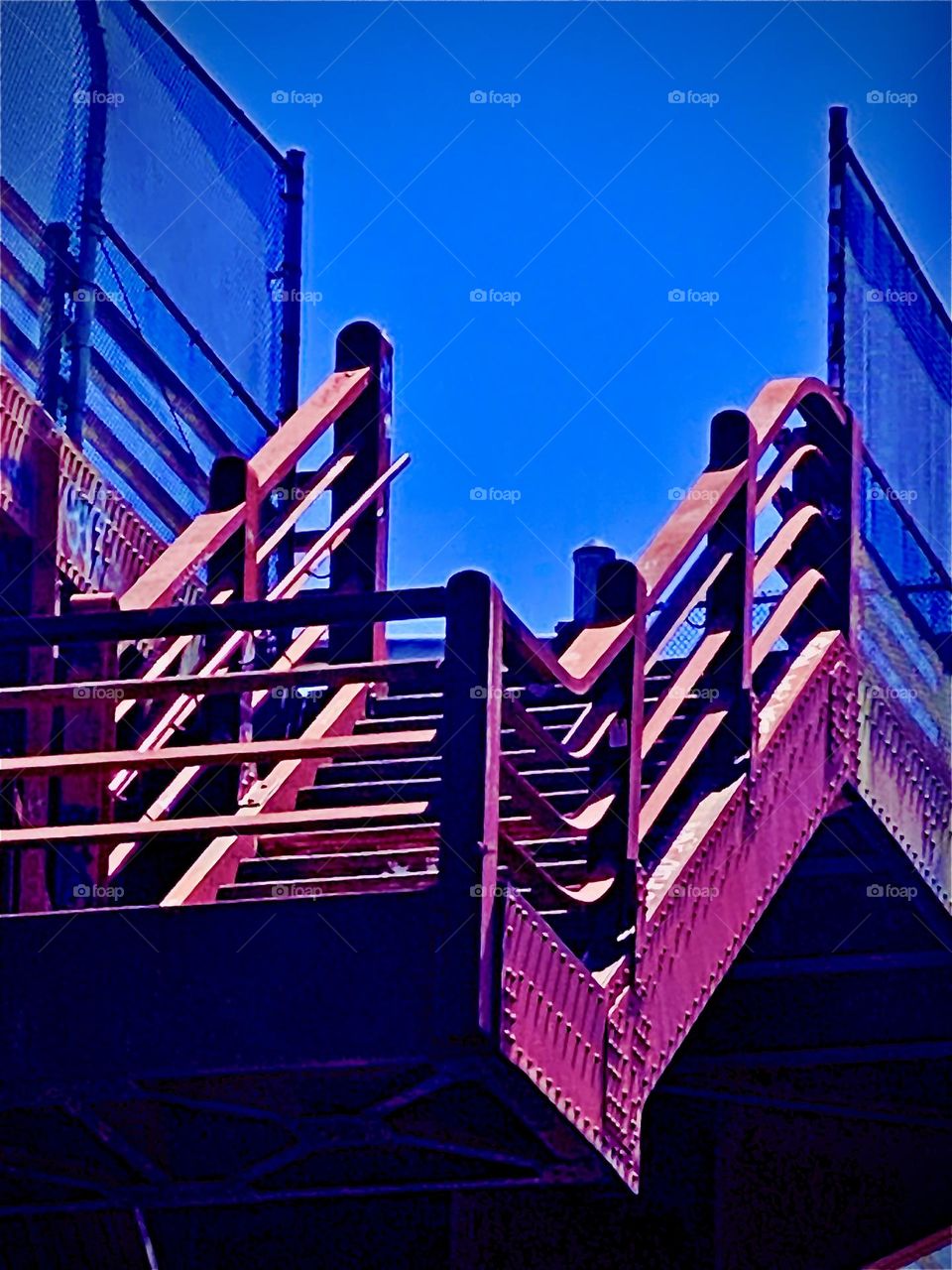 The red metal staircase leads up to the „Pulaski Bridge“ that spans the E River at „Newtown Creek“ from LIC, Queens to Greenpoint, Bklyn. Pedestrians ascend this way to walk over the bridge in their own lane. 2022. Hypnotic Productions