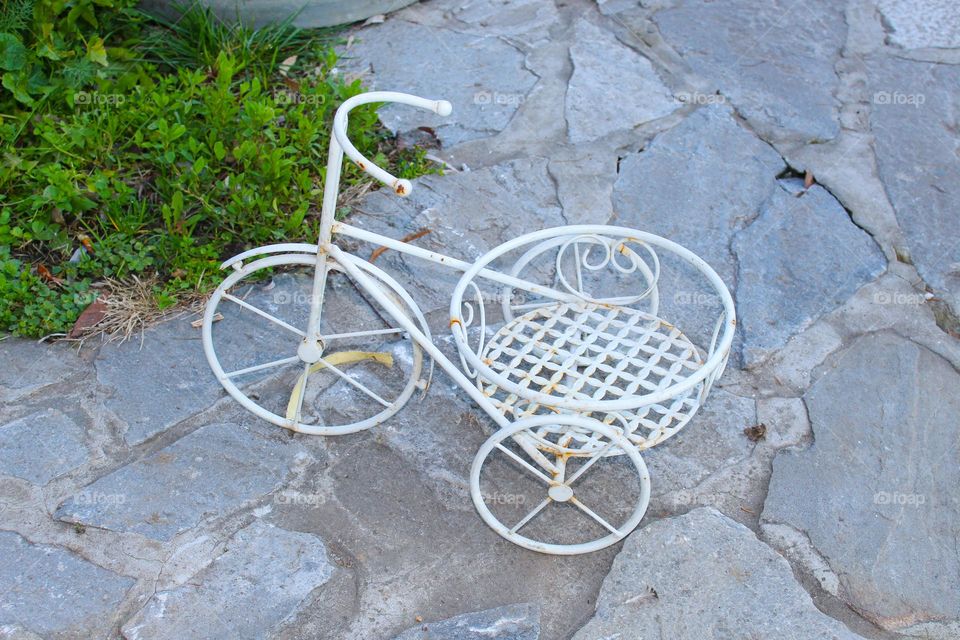 A small white metal bicycle that serves as a pot holder on a stone surface.  Decorative bicycle