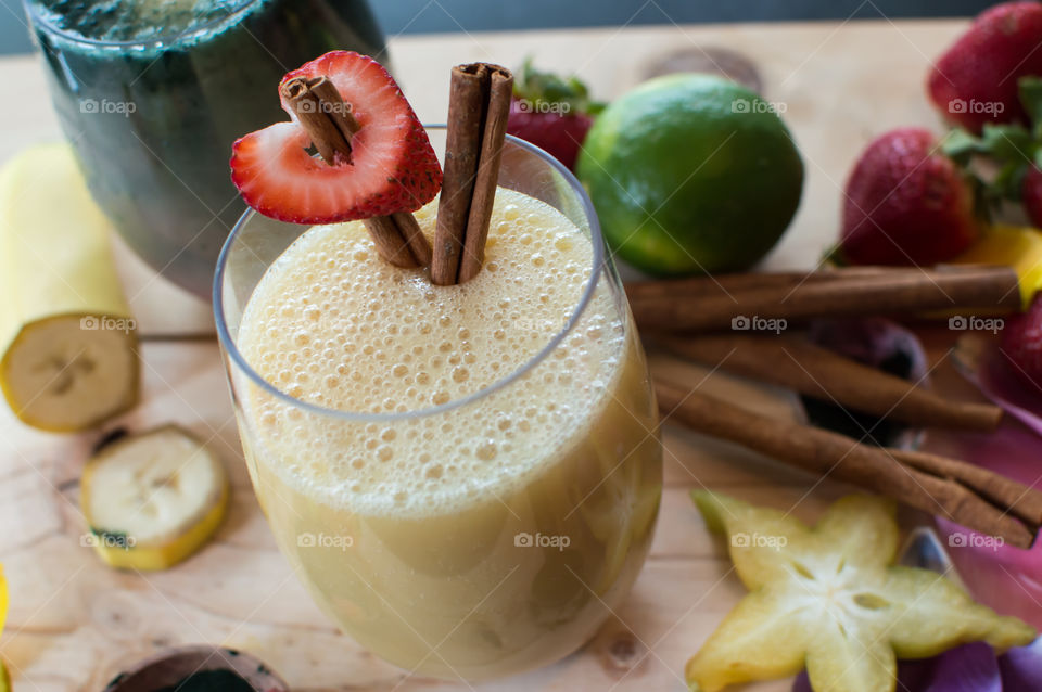 Making smoothies high angle view of heart shaped strawberry on cinnamon sticks in bubbly white smoothie with green smoothie and fresh fruit ingredients in background