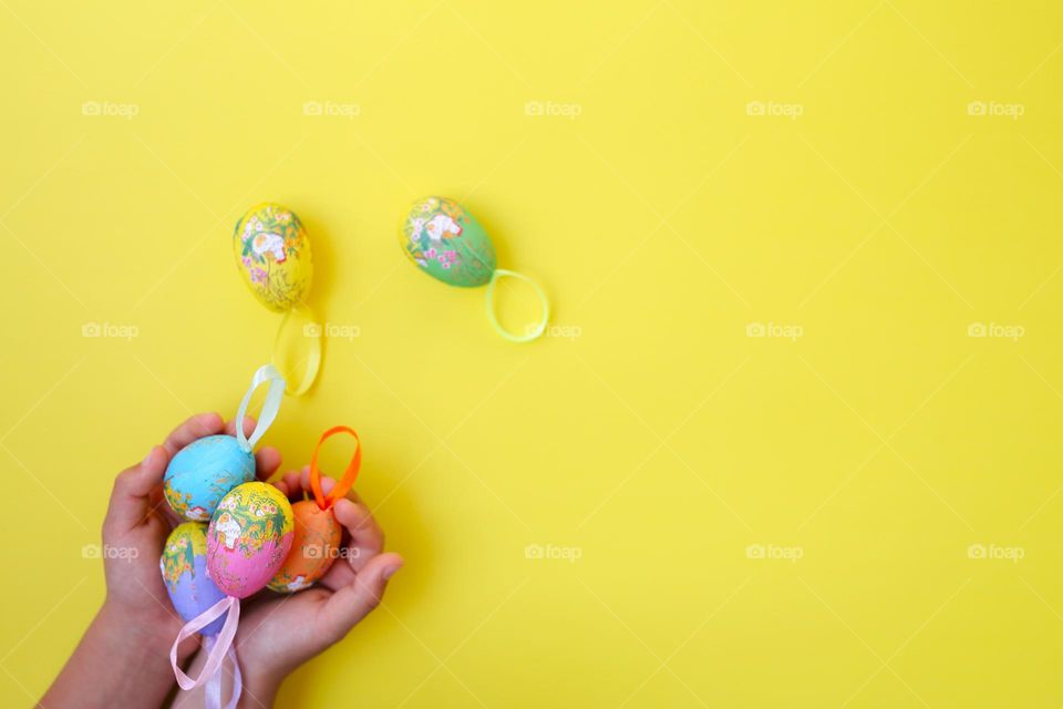 beautiful Easter eggs on a yellow background, top view, eggs in children's hands, handmade