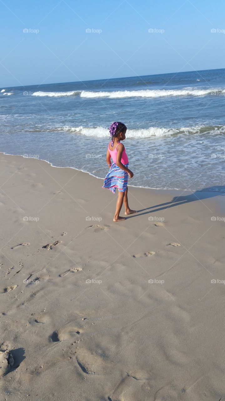 Price less. Grand daughter strolling along the beach enjoying the cool waters on a sunny day.
