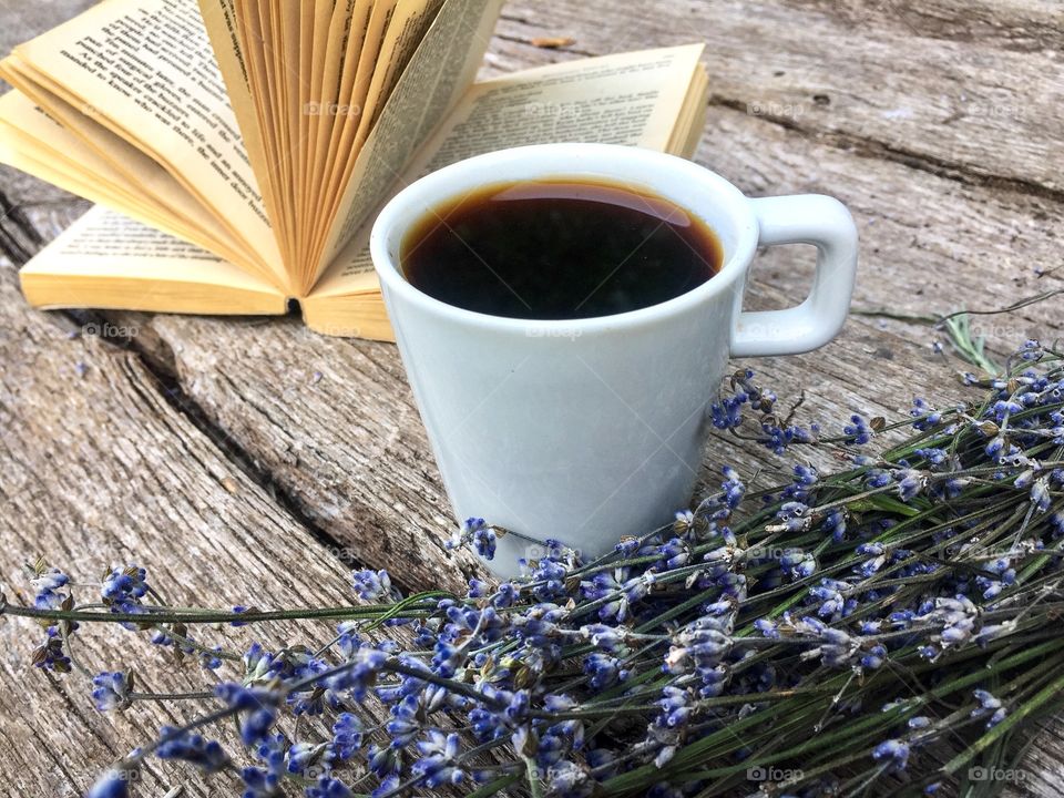 Open book with lavender and cup of coffee beside placed on wooden table