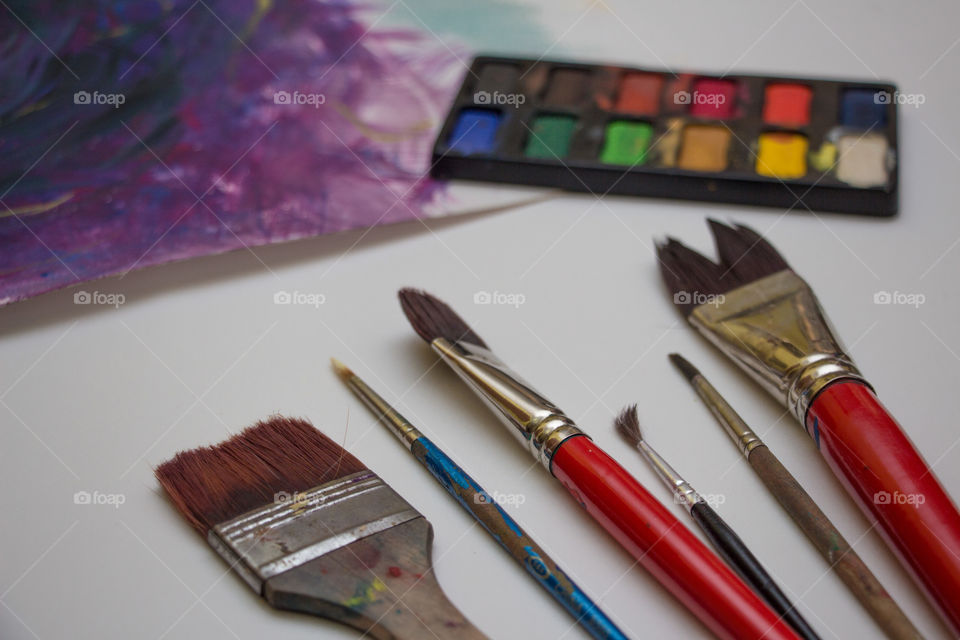 Brush tools beside a finished paint and gouache colors.