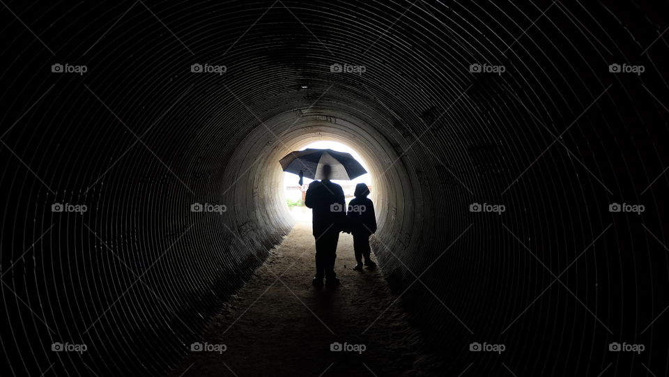 Silhouette of father and son finding shelter from rain in a tunnel.