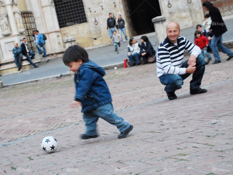 Proud papa. A proud father watches his toddler son play with a soccer ball 