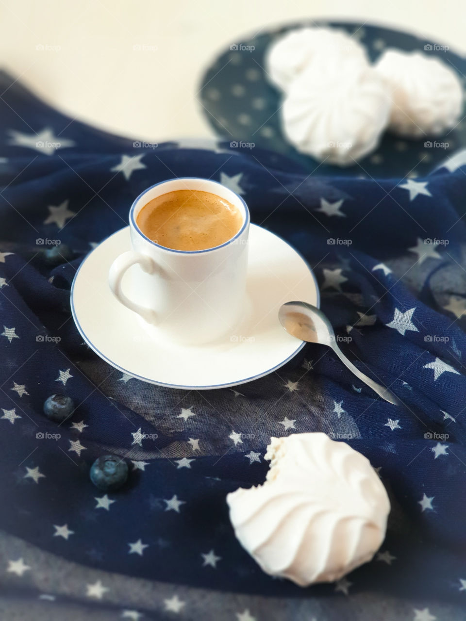 Freshly brewed coffee with white marshmallows on a blue textile tablecloth with stars.  A sweet snack with a cup of espresso.  A nice start to the day