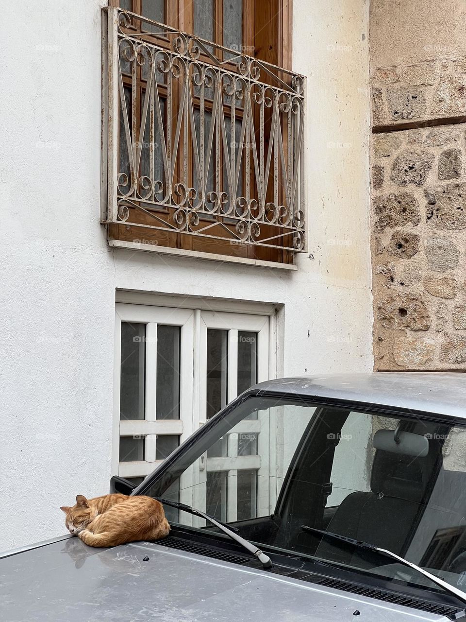 Red cat sleeping on the vintage gray car in the old city centre 