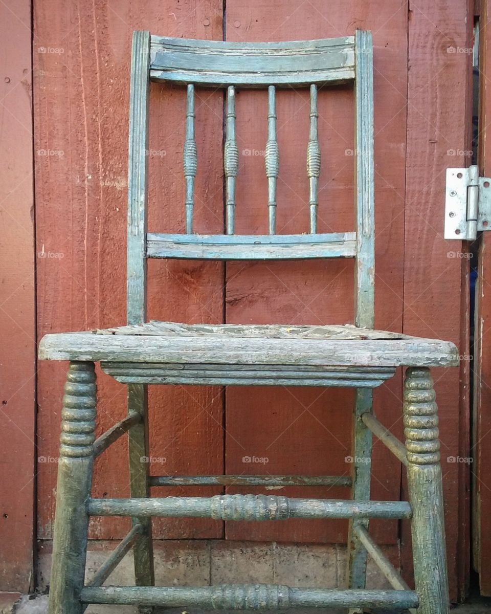 weathered chair with red stained fence background
