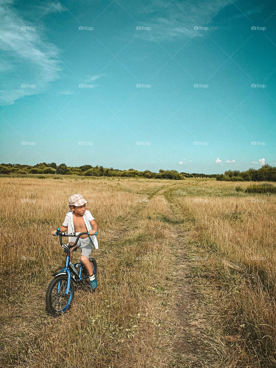 Freedom concept child boy rides a bike across the field, summer in the village