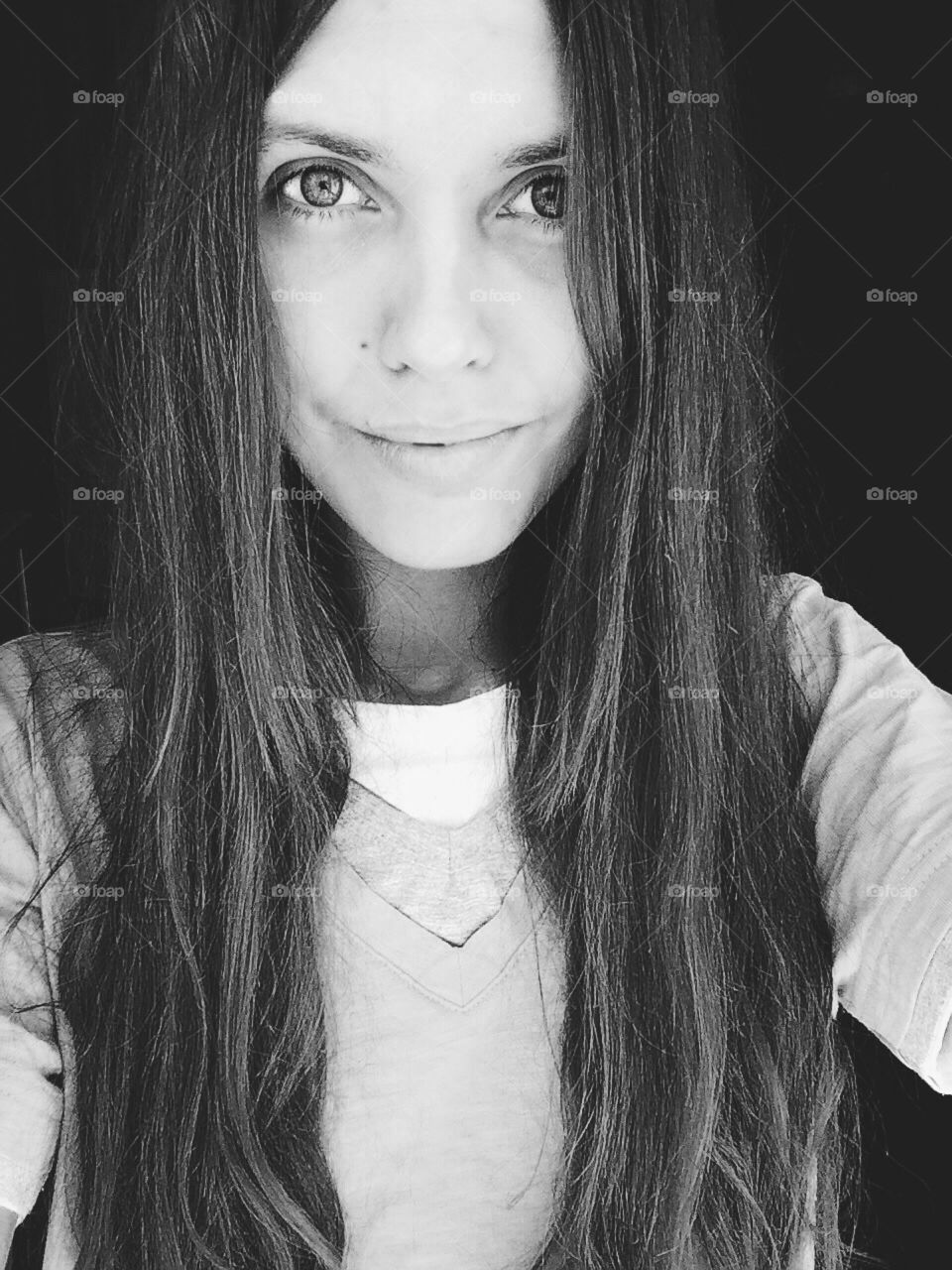 Black and white selfie portrait of a girl with long dark hair and big eyes and full lips staring at you and smiling