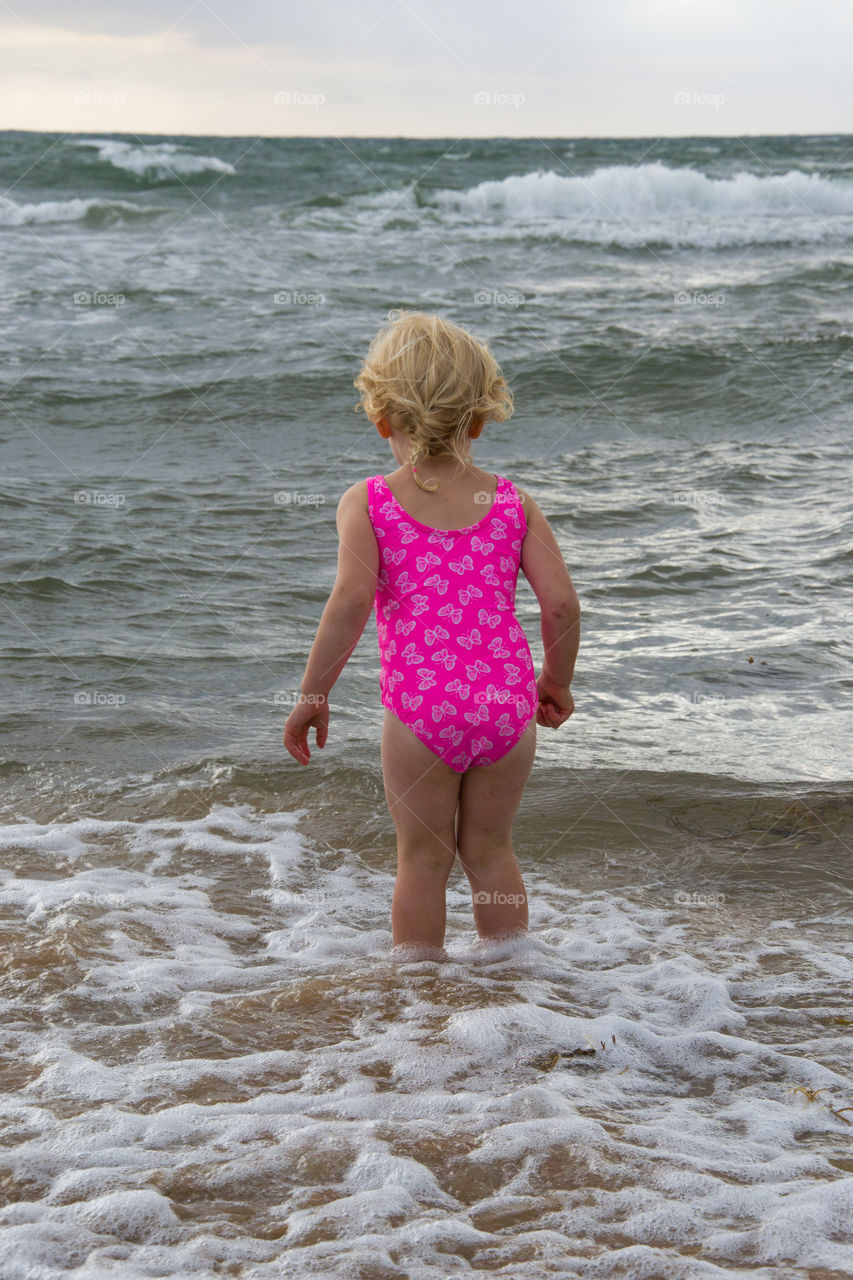 Little girl playing at the beach of Tylösand outside Halmstad in Sweden. It's about to get stormy weather but the girl is having fun swimming and playing in the water.