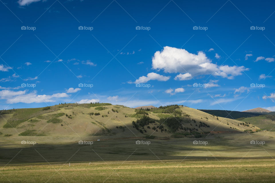 A cloud-dappled view of the Colorado plains, with foothills and blue sky in the background.