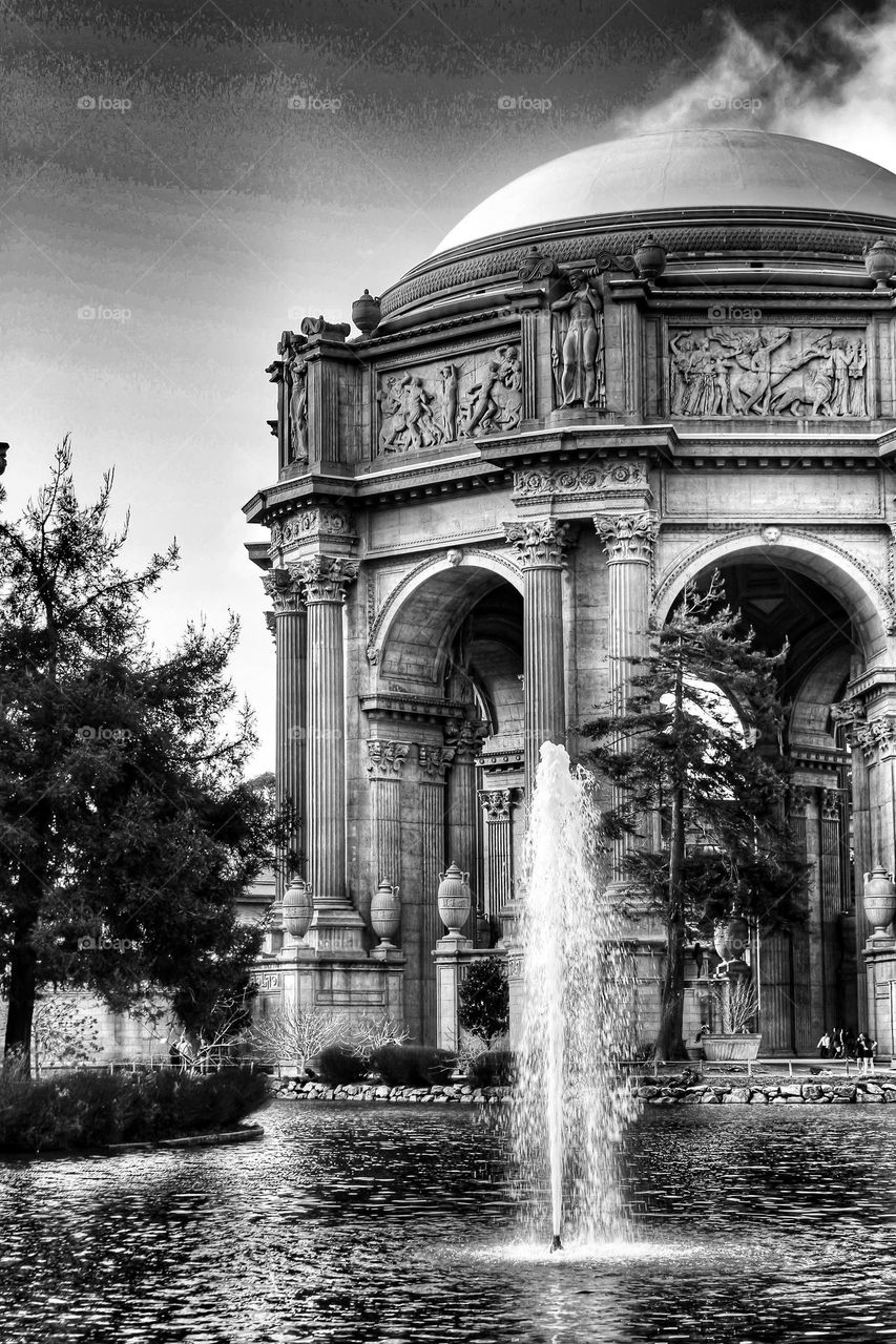 Vintage looking black and white image of the landmark Palace of Fine Arts in San Francisco California with the fountain rising through the lagoon on a warm sunny afternoon with clouds in the sky 