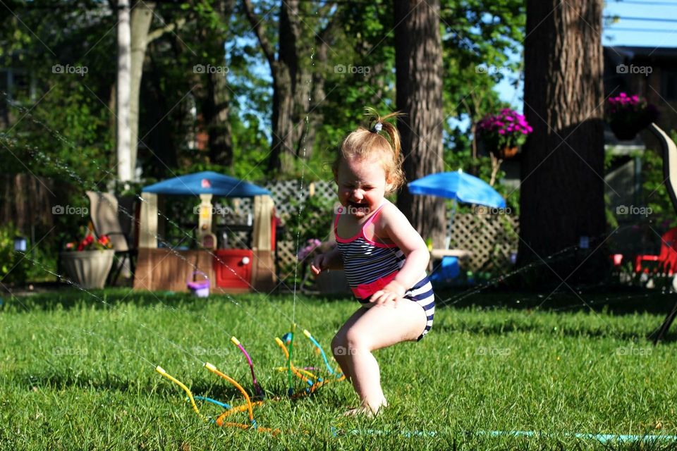 Child playing with a water sprinklers in the grass 