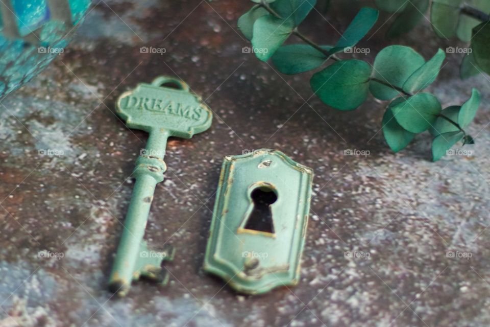 Light teal, metal vintage key with embossed word, “Dreams,” and keyhole on concrete surface 