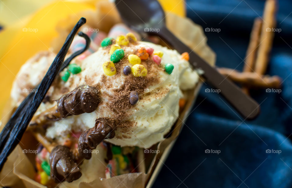 Fun vanilla ice cream bowl with scoops of vanilla ice cream garnished with vanilla bean pods and chocolate covered pretzels with rainbow sprinkles for festive occasion or party sundae dessert 