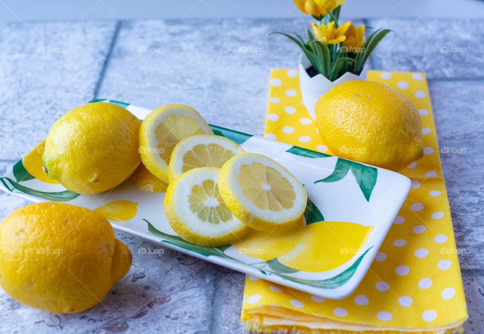 A colorful display of whole and sliced lemons on a tile countertop with a yellow napkin and yellow flowers