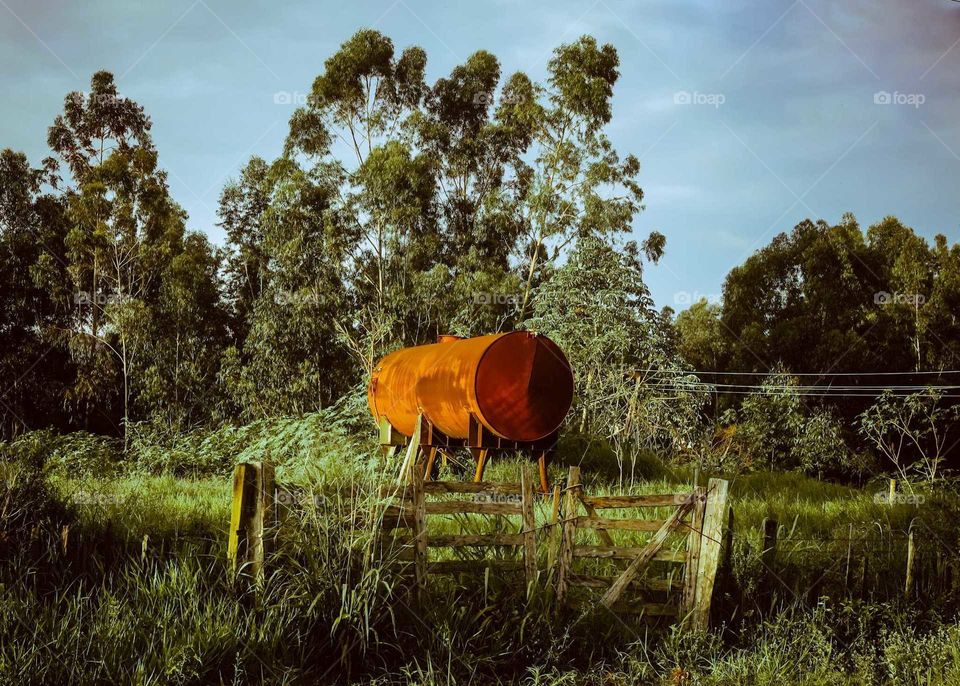 Beautiful farm rusty metal structure, rusty orange iron water tower, at fields. There is a wooden gate at the front, beautiful blue sky, trippy colors