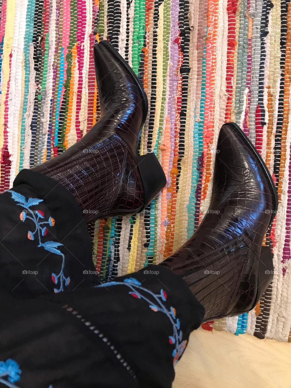 These boots were made for walking . Shiny pounted, brown ,snakeskin effect, pointed boots . Sideways shot. Bright striped rug
