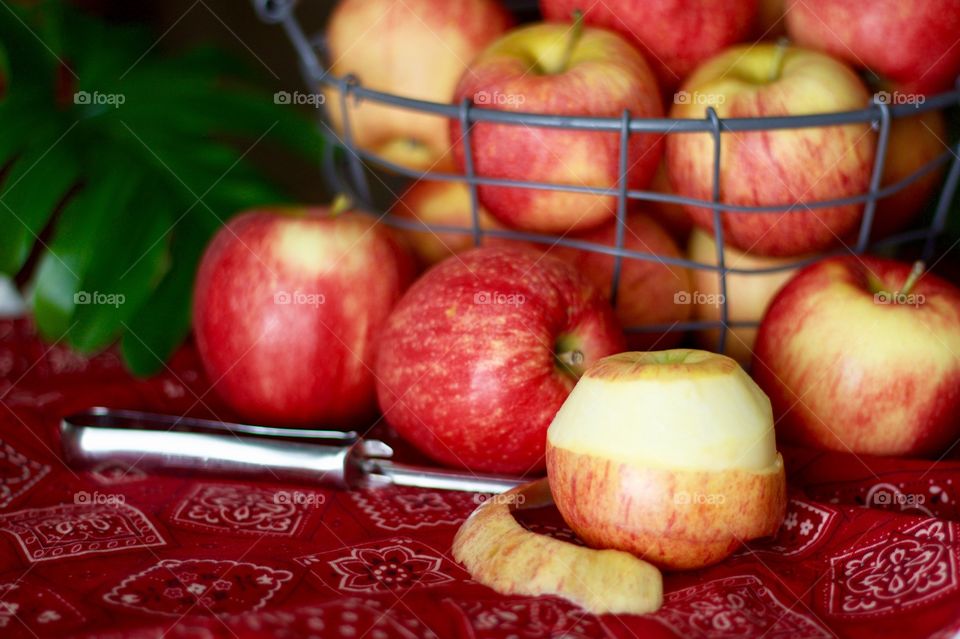 Fruits - Gala apples in a wire basket with a partially peeled apple and peeler on a red bandana-print tablecloth