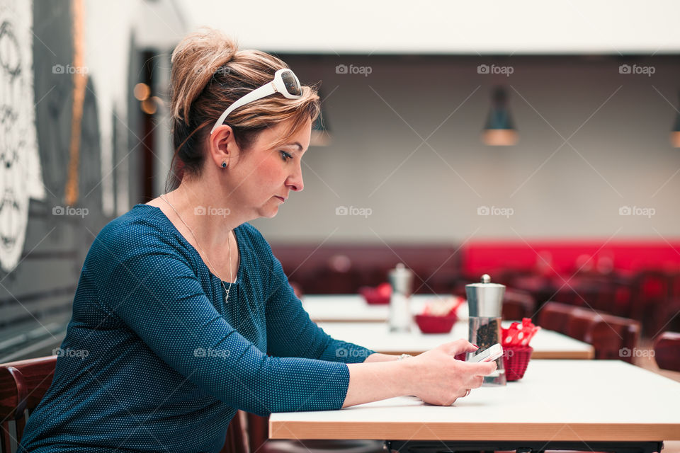 Young woman using mobile phone sitting by a table in cafe