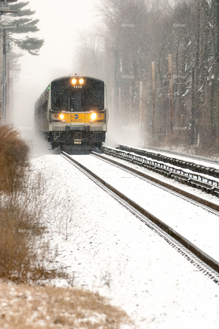 A commuter train approaching a station in a snowy winter scene. 