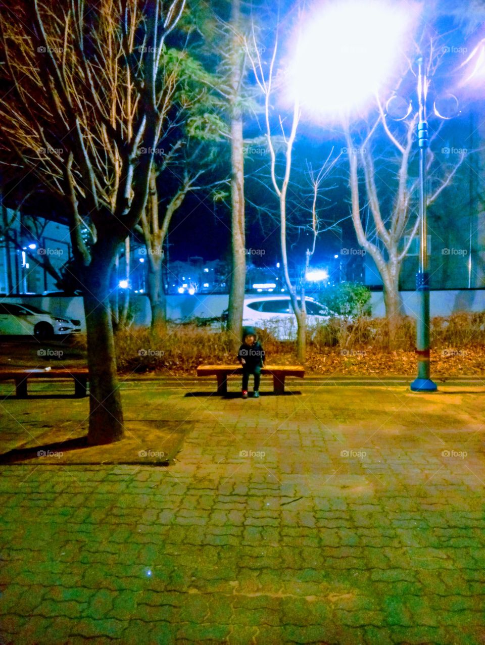 The night at the Country Park.
a little boy sitting on the bench.
he loves the scenery of the quite place with wide grounds and lots of trees around it.