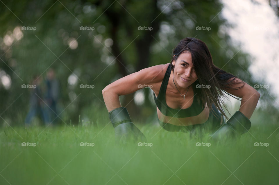a beautiful, athletic brunette, in a black sports suit, in boxing puppies, is lifted off the ground.  activities outside the home, in the park.  strong, stylish woman
