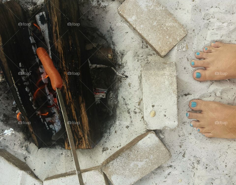 Woman's toes by beach campfire with hot dog