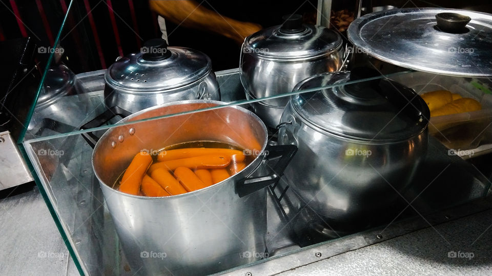 Caldeirões de inox e alumínio com salsichas em água quente para o preparo de hot dog.