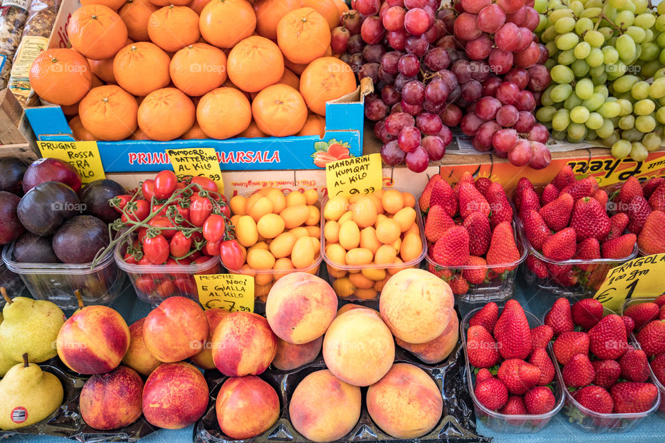Variety of colorful fresh juicy fruits in the baskets on grocery market. Oranges, peaches, strawberries, pears, nectarines, mandarins, kum quats, tomatoes, plums, green grape, red grape.