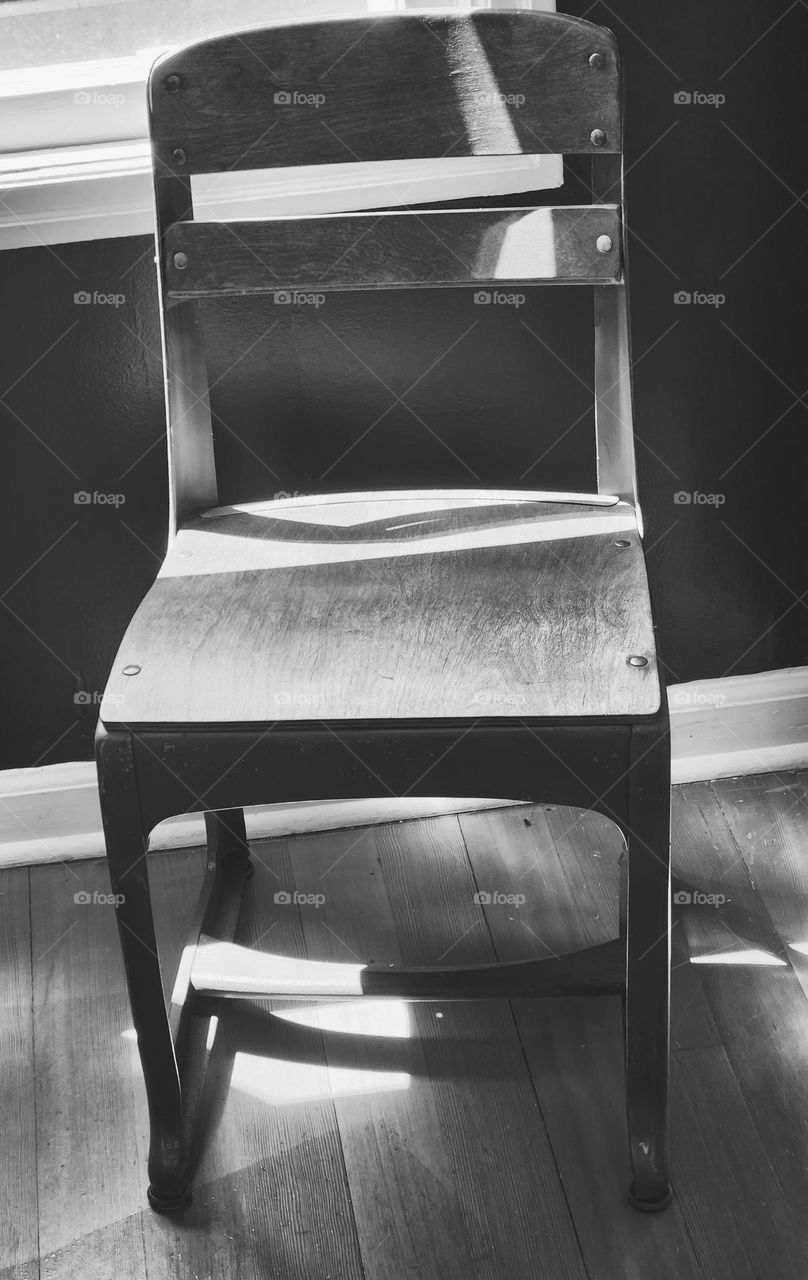 an old fashioned wooden school chair in black and white with the light from a window shining on it