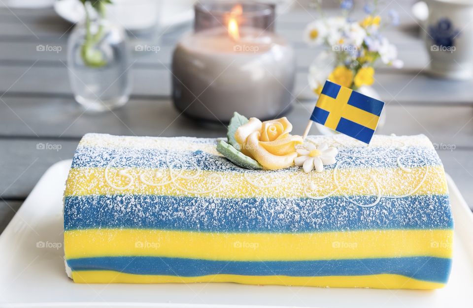 Closeup of a delicious yellow blue striped marzipan cake decorated with flowers and a Swedish flag, celebrating midsummer 