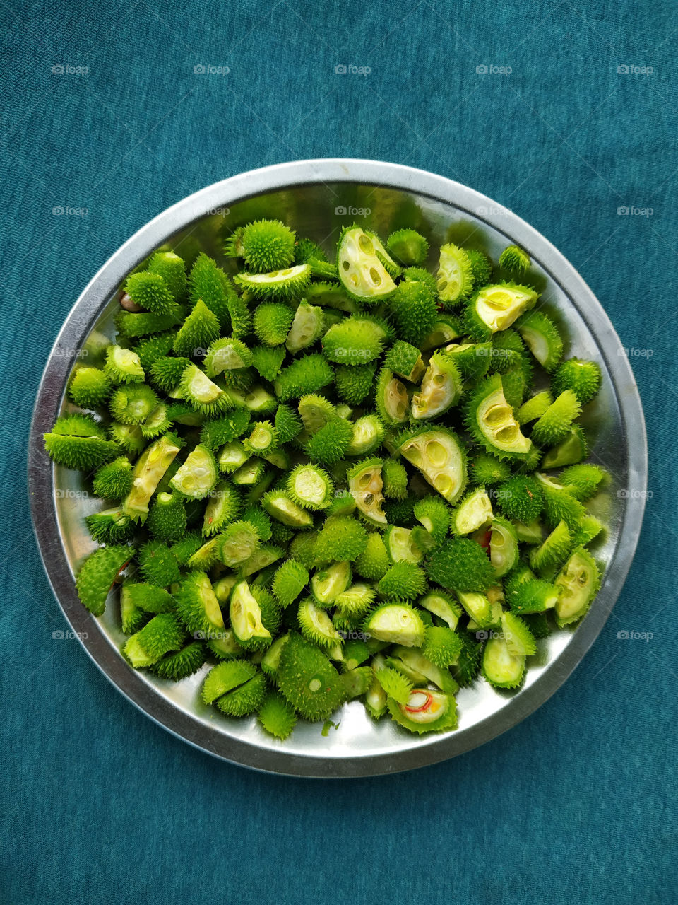 Spiny gourd in small pieces in steel plate on teal background
