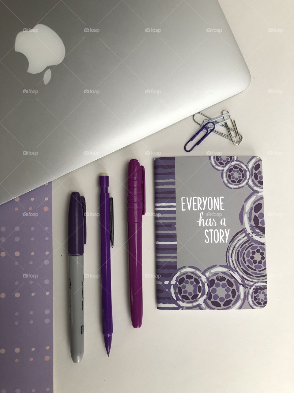 A flat lay themed in purple and mold with a laptop and a notebook with a motivational sayings on it