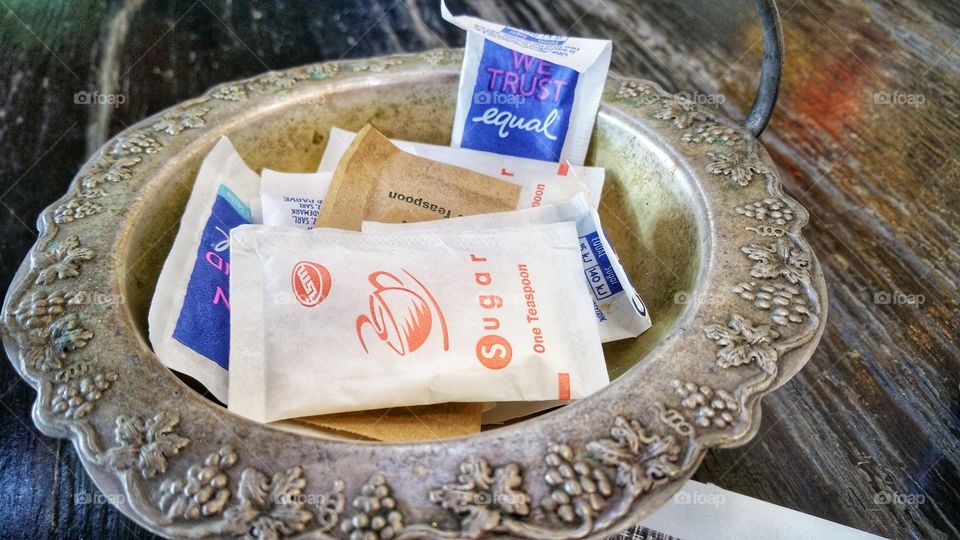 Ornate silver table pot containing sachets of refined white sugar, raw sugar and artificial sweetener (Equal). Mainly provided for coffee and tea drinkers.
